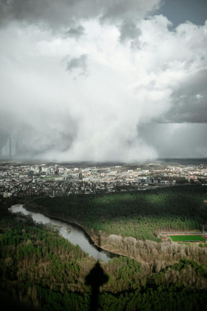 A panoramic cityscape view with a river under a dramatic overcast sky. Shadow of a tower visible.